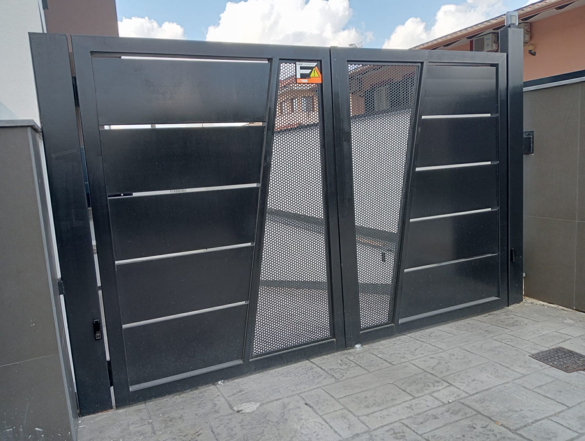 Un moderno cancello carrabile a doppia anta in metallo nero con pannelli orizzontali pieni e sezioni centrali in rete decorativa.