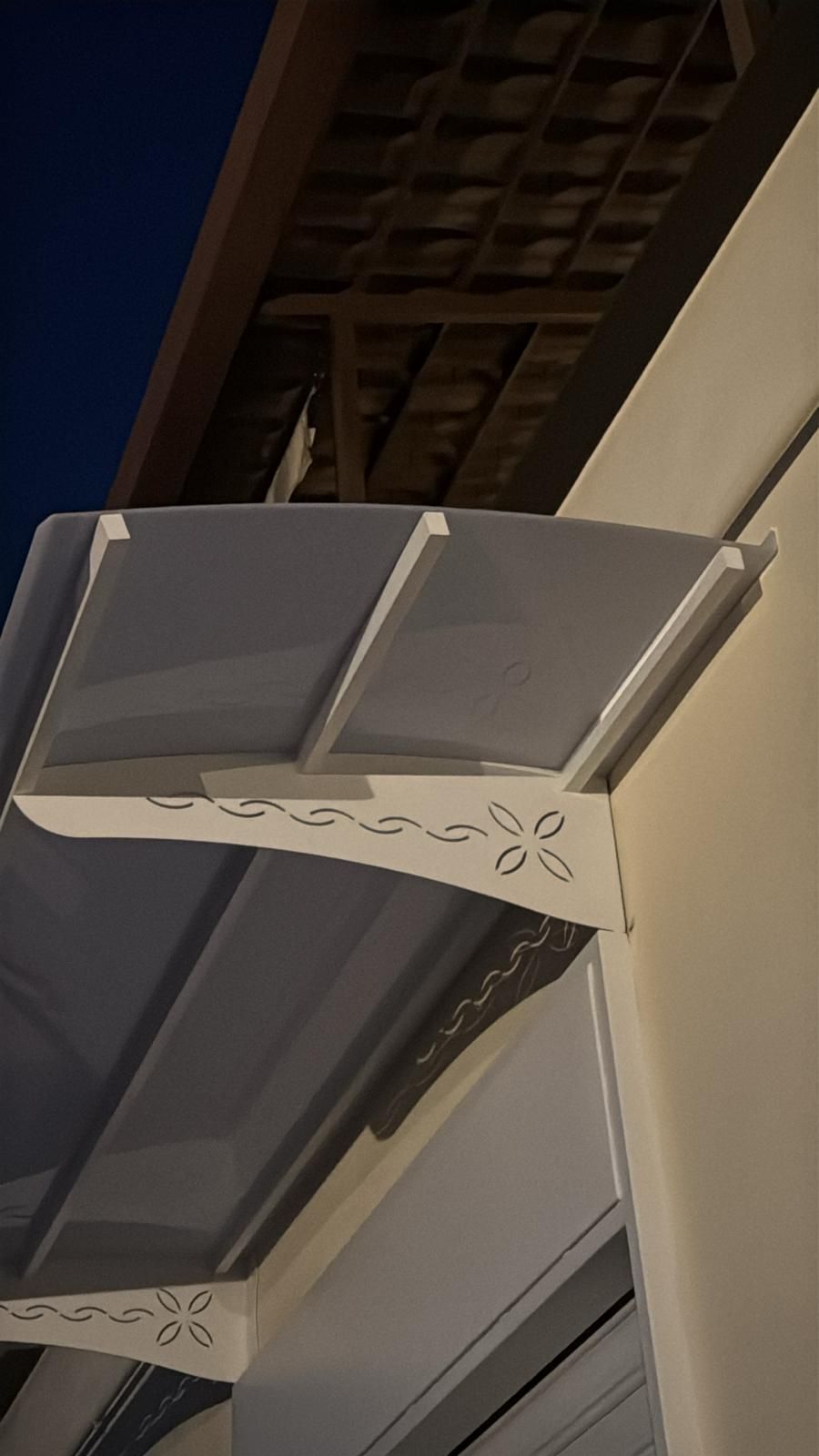 Una moderna tettoia ad arco per l'ingresso, con staffe decorative bianche e un pannello grigio traslucido, che sovrasta la facciata di un edificio.