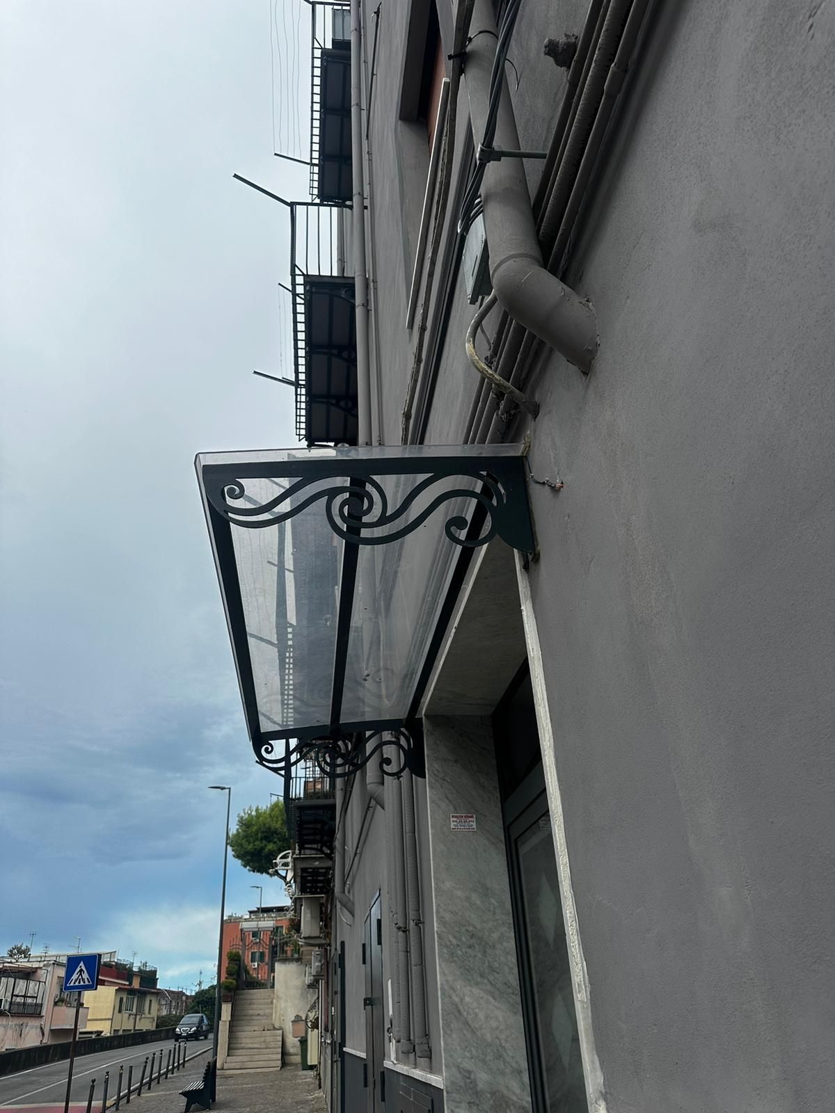 Vista dal basso dell'esterno di un edificio grigio con una tettoia in metallo nero con copertura in vetro sopra un ingresso.