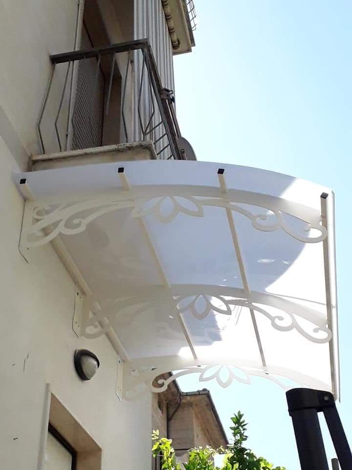 Tenda bianca curva con decorazioni a volute, montata sopra l'ingresso di un edificio e un balcone esposto alla luce del sole.