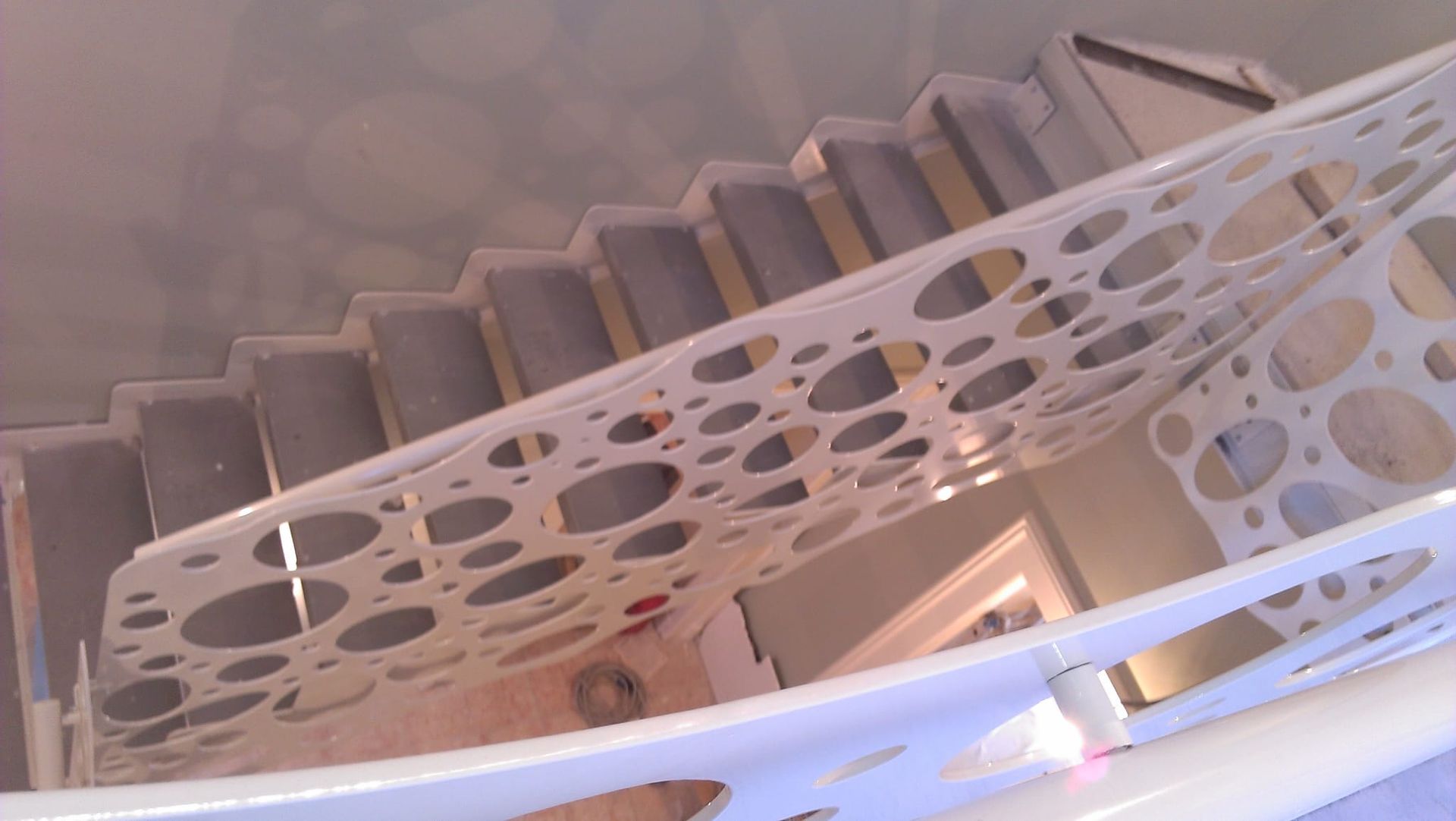 Una scala con gradini rivestiti di moquette grigia, racchiusa da una ringhiera bianca caratterizzata da un moderno motivo a intagli circolari.