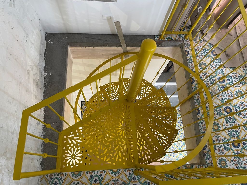 Una vista dall'alto di una scala a chiocciola di un giallo brillante con intagli decorativi elaborati sui gradini.