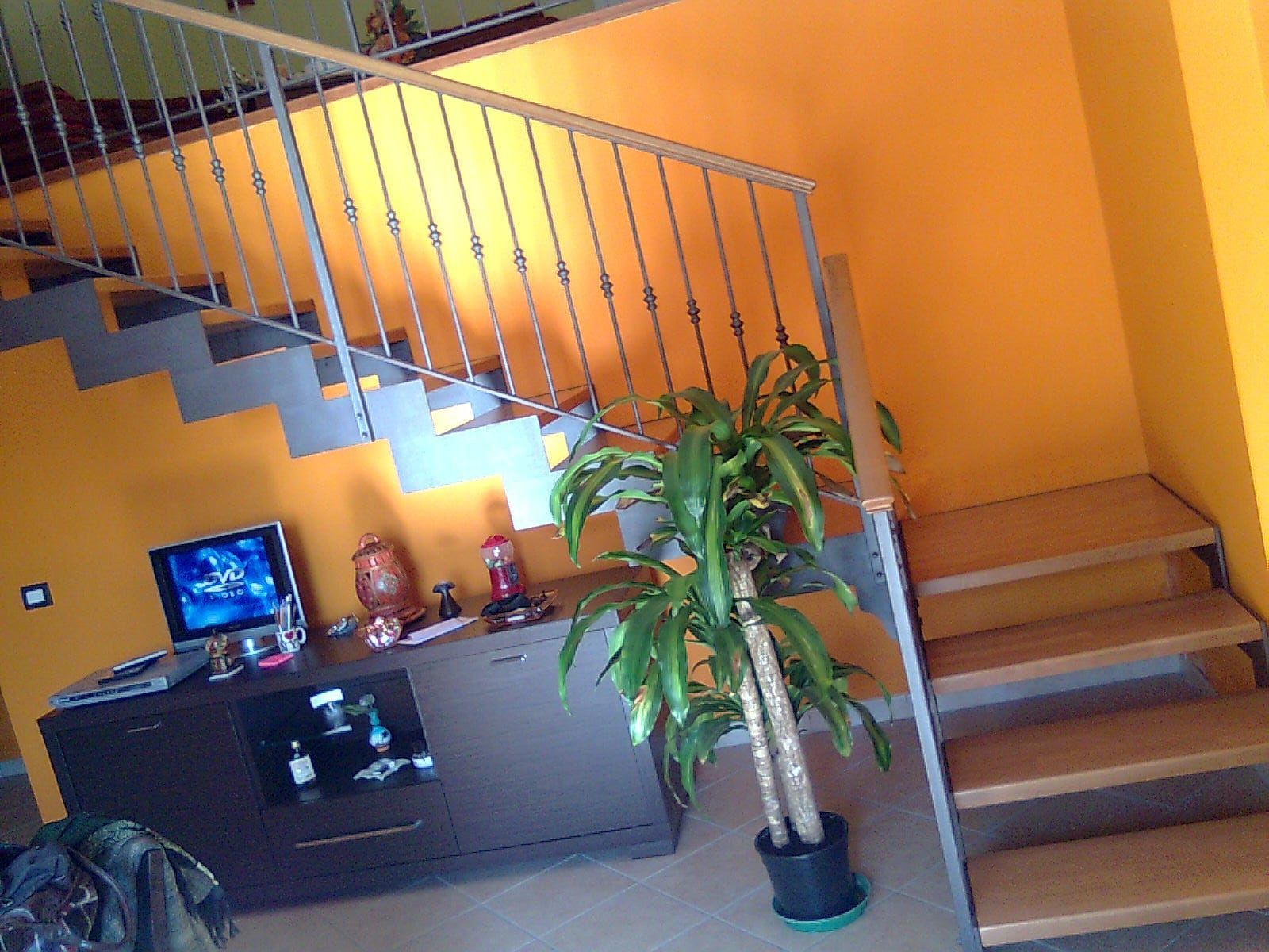 Un soggiorno caratterizzato da pareti arancioni brillanti, una scala in legno, una pianta in vaso e un mobile porta TV con apparecchi elettronici.
