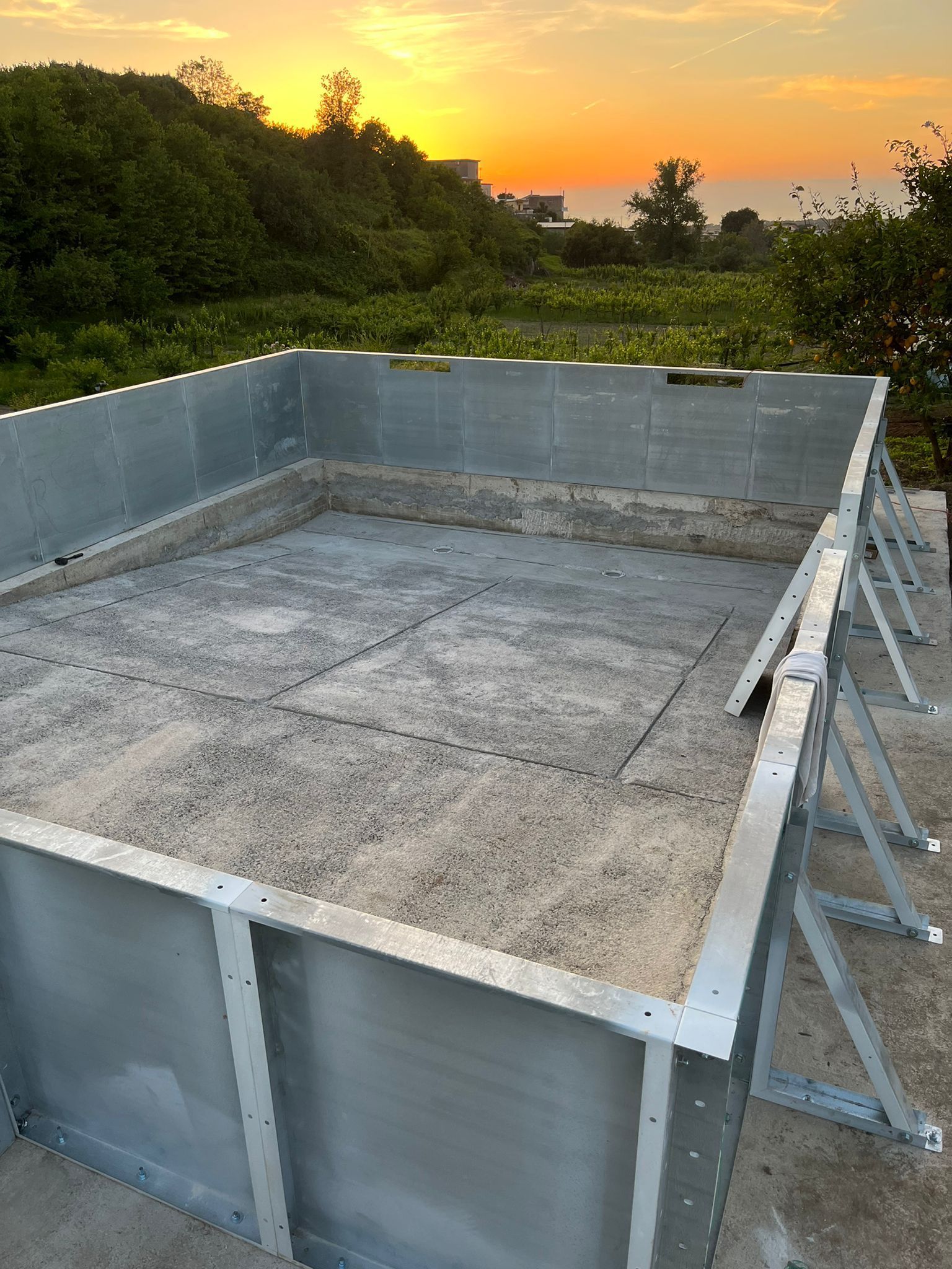 Una struttura rettangolare composta da pannelli di acciaio zincato, poggiata su una base di cemento, al tramonto.