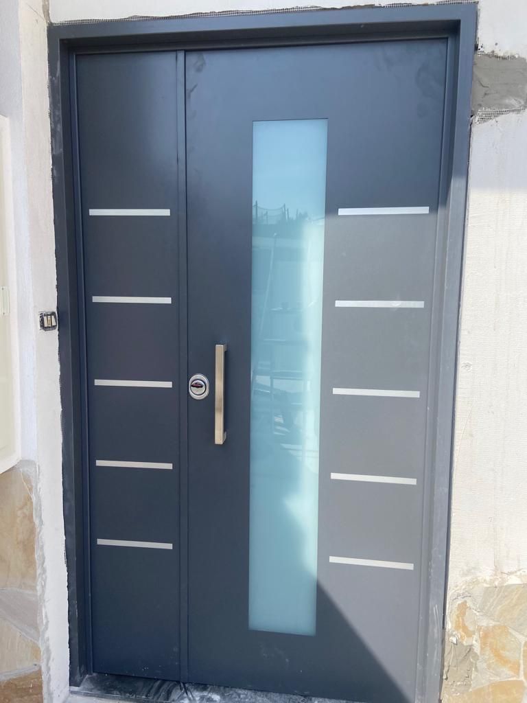 Una moderna porta esterna grigio scuro con inserti metallici orizzontali, un pannello verticale in vetro satinato e una maniglia in metallo.