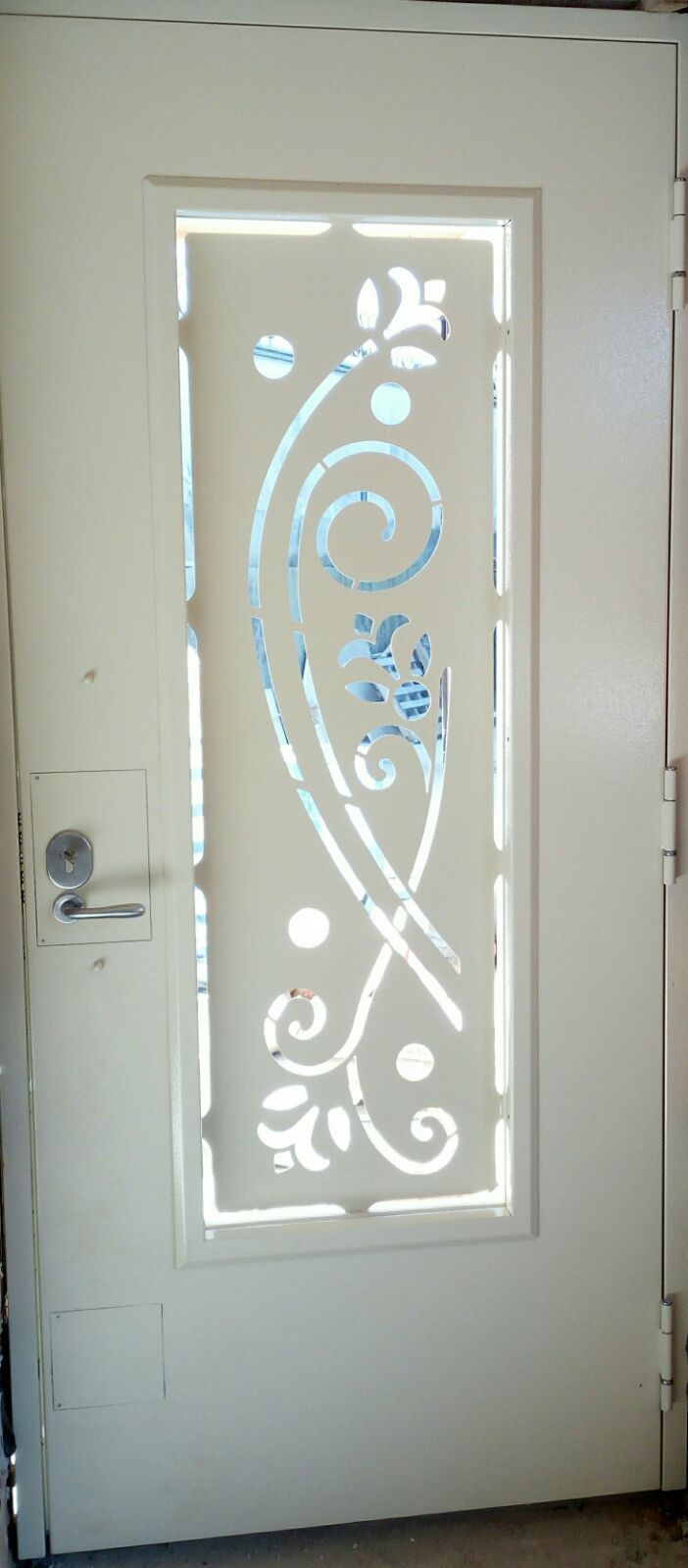 Porta color avorio sporco con pannello verticale tagliato al laser, decorato con motivi floreali e a volute su sfondo di vetro satinato.