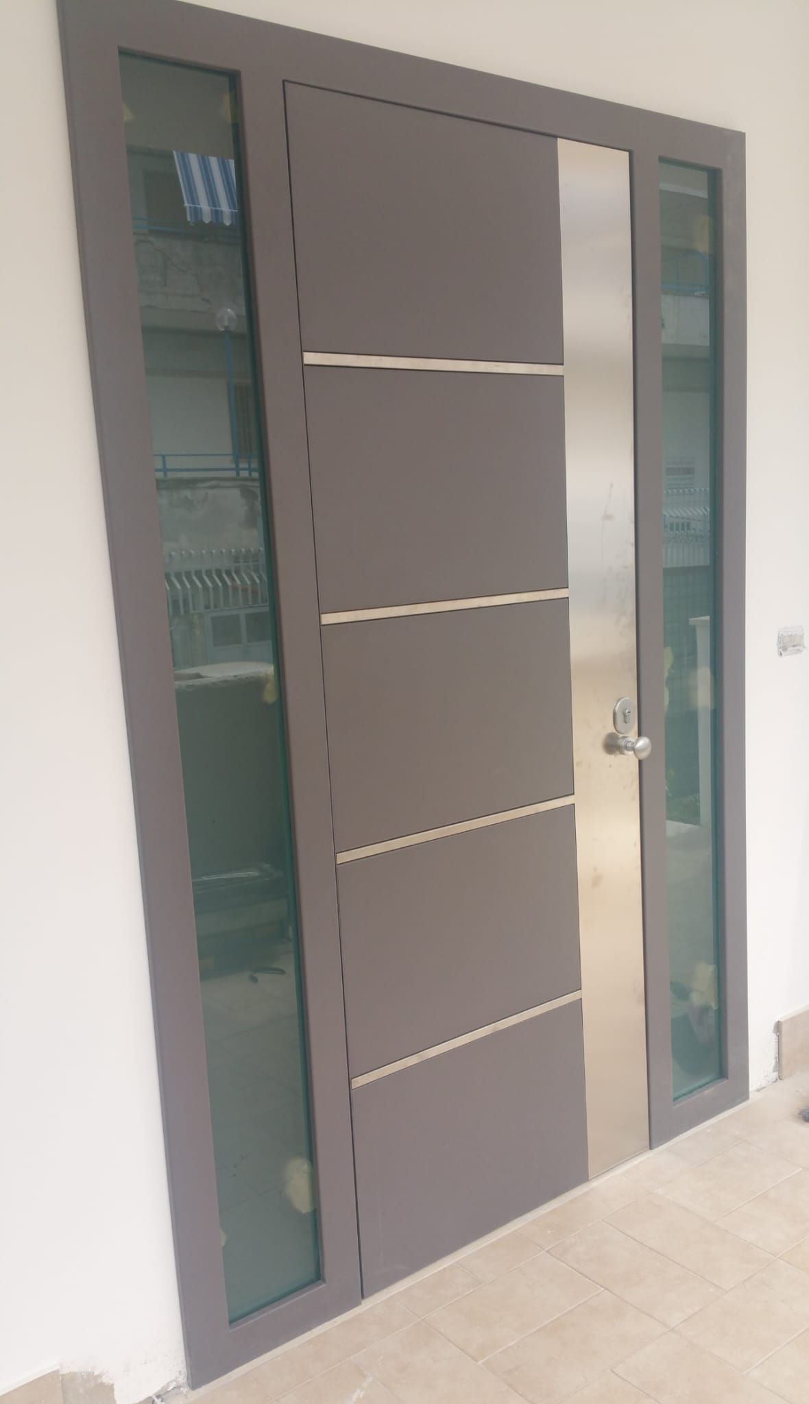 Una moderna porta d'ingresso grigia con un pannello di vetro verticale su ciascun lato e inserti orizzontali argentati sulla superficie.