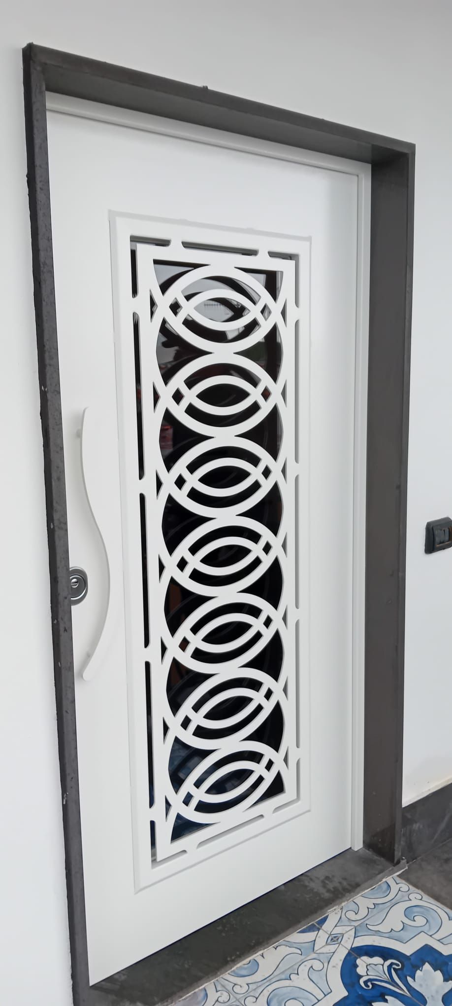 Una porta bianca con cornice scura caratterizzata da un motivo decorativo verticale intagliato, formato da ovali bianchi intrecciati.