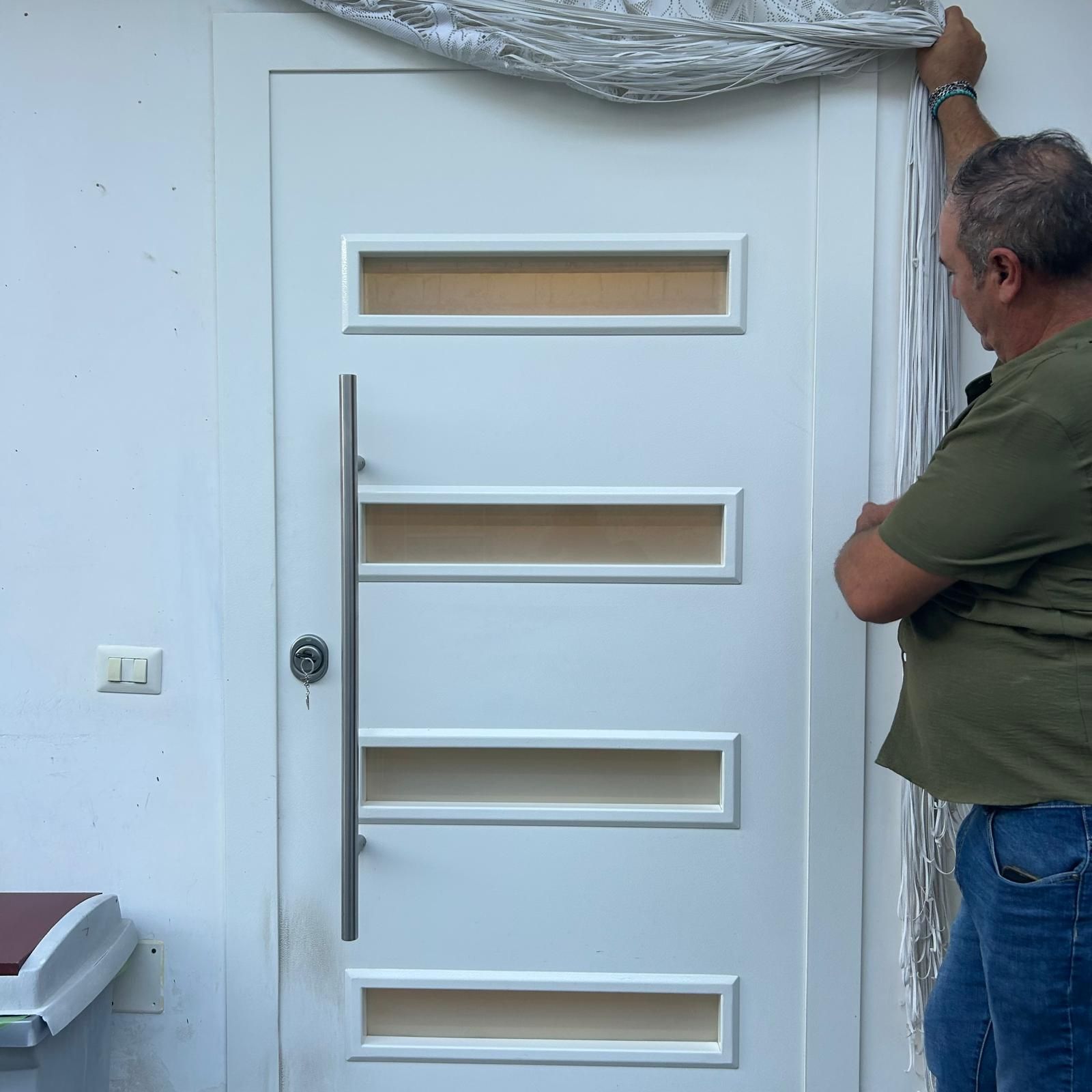 Una persona installa una zanzariera argentata sopra una porta bianca con quattro pannelli di vetro orizzontali.