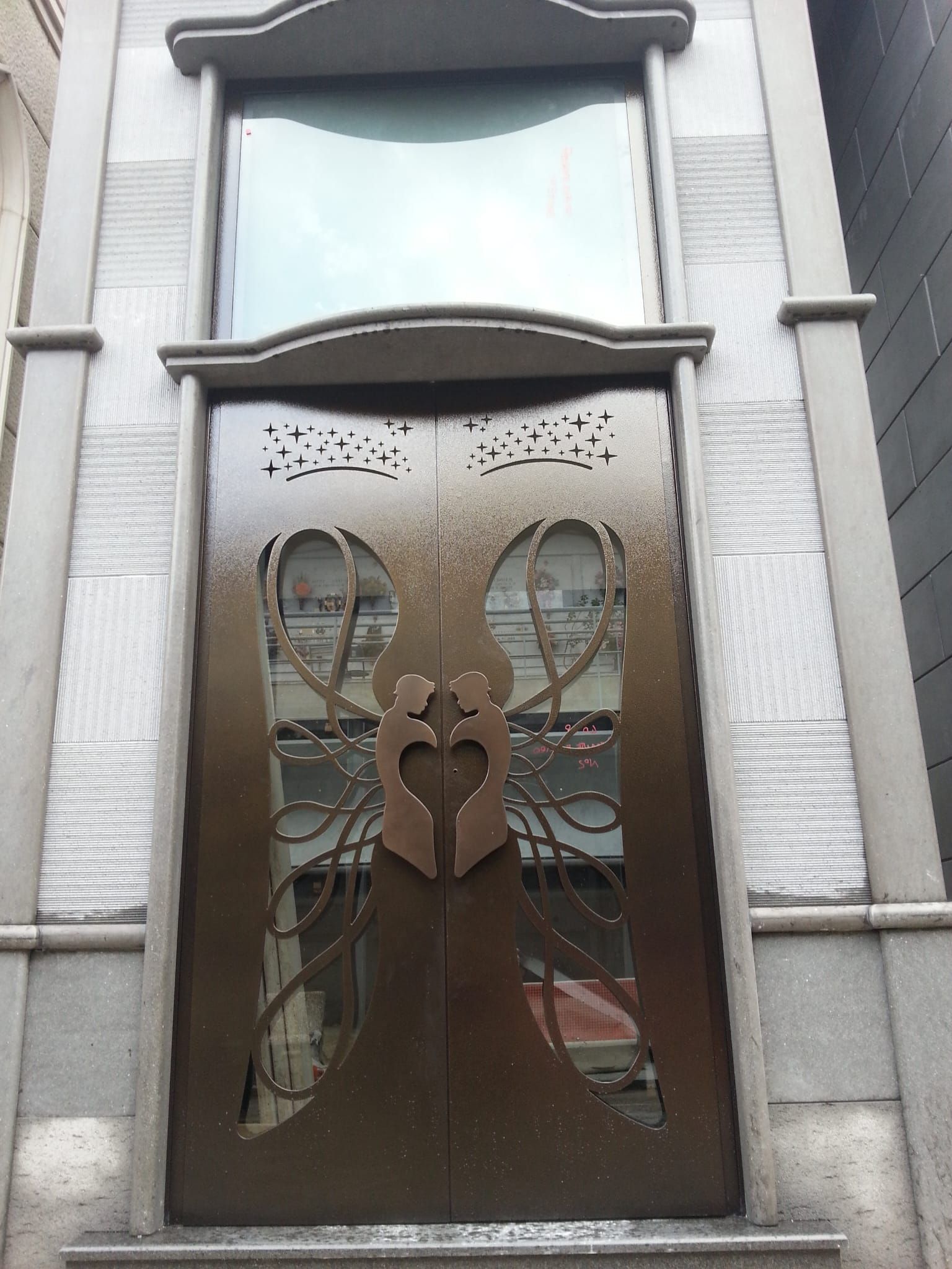 Doppie porte decorative color bronzo con una sagoma intagliata di due figure che si abbracciano, incastonate in un ingresso in pietra.