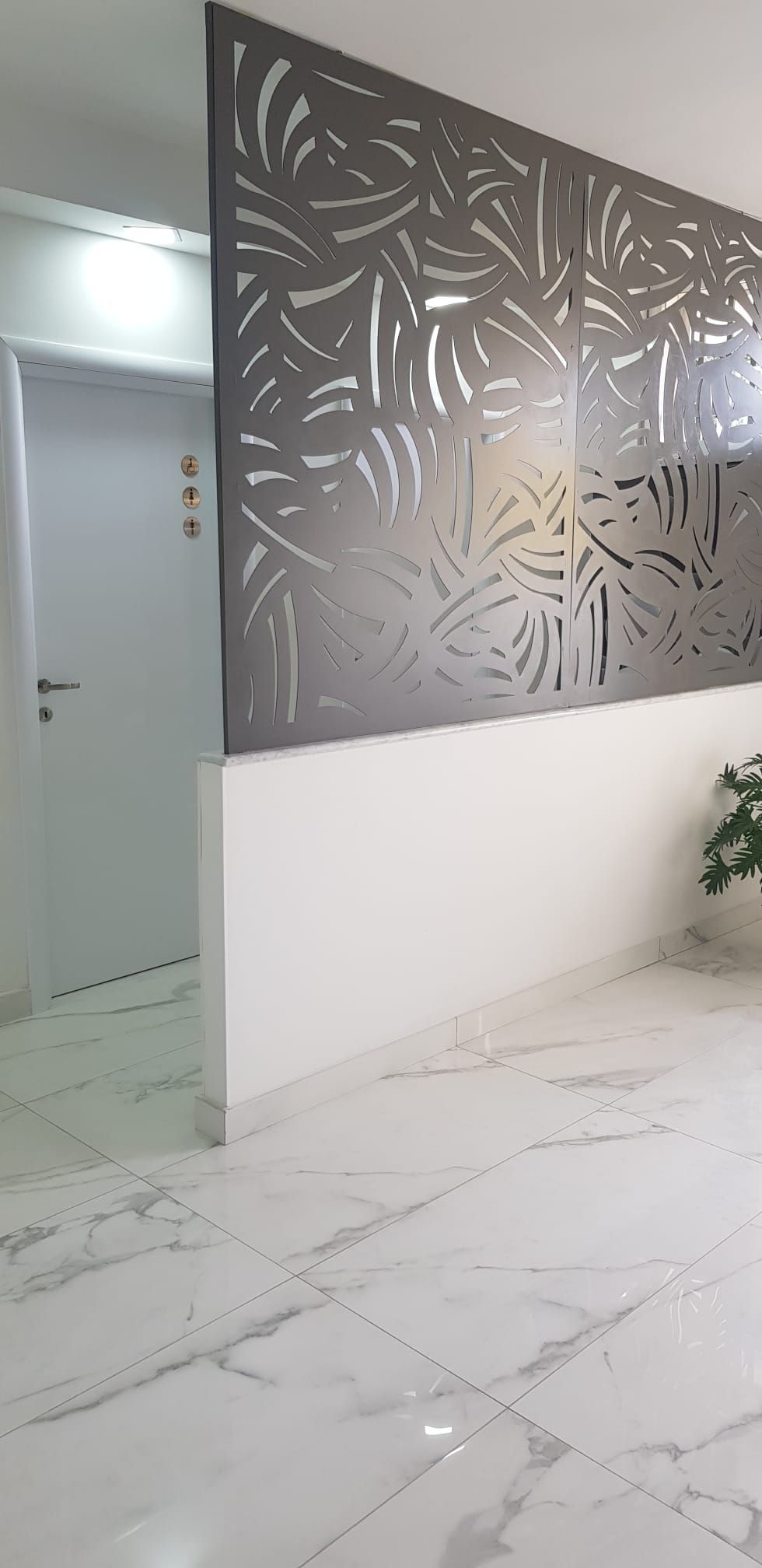 Un pannello decorativo in vetro marrone scuro, tagliato al laser, montato su un muretto bianco in una stanza con pavimento in marmo bianco.