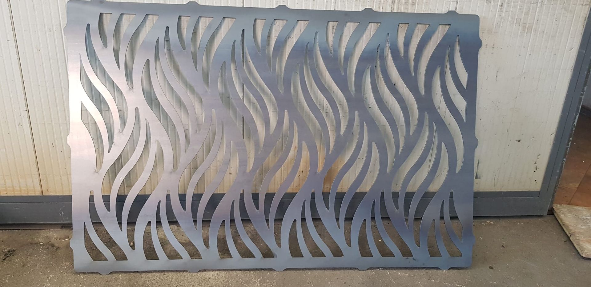 Un paravento decorativo rettangolare in metallo con un motivo a fiamma o organico verticale, tagliato al laser, in grigio opaco.
