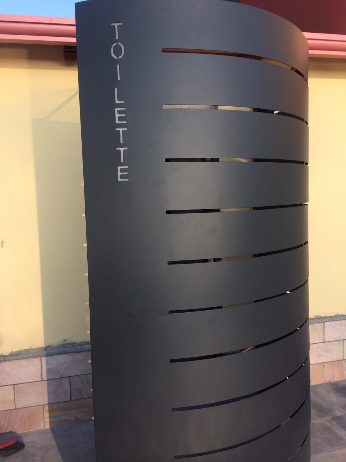 Un moderno cartello metallico curvo, di colore grigio scuro, con la scritta