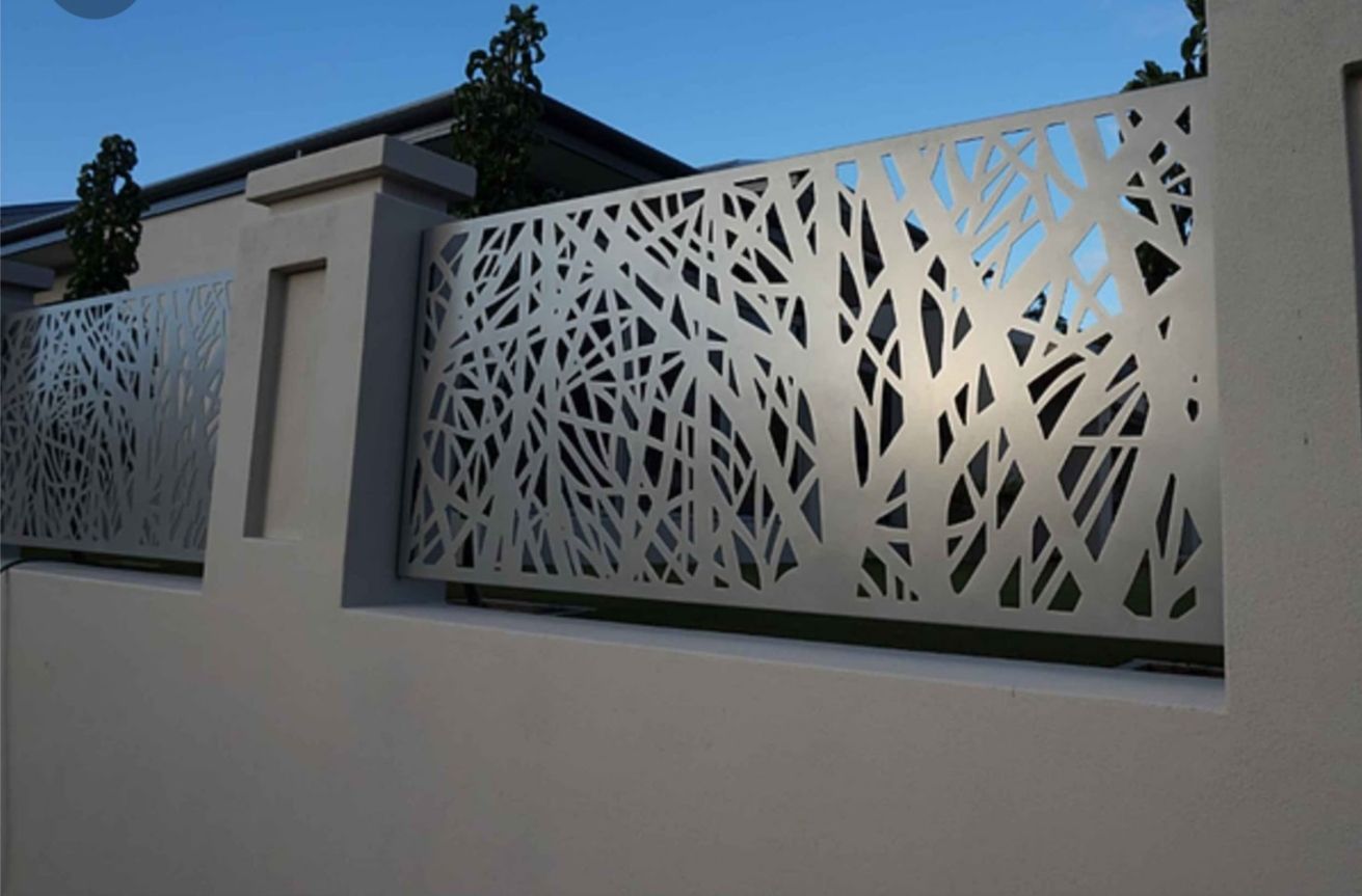 Un pannello decorativo in metallo per recinzione, con un intricato motivo a rami d'albero organici tagliato al laser, montato su una parete in stucco bianco.