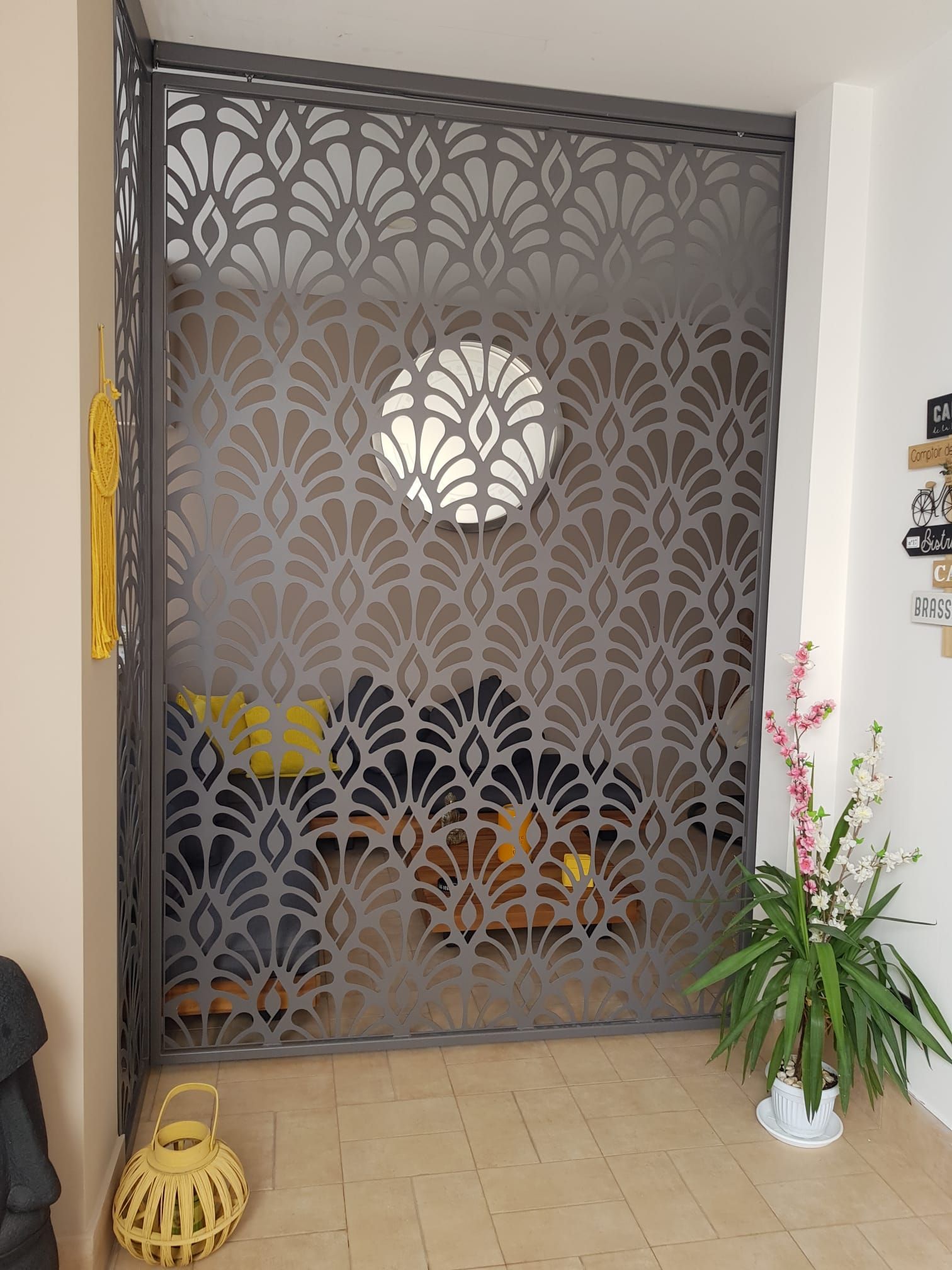 Nell'ingresso, accanto a una pianta, si trova un divisorio decorativo in metallo grigio, tagliato al laser e caratterizzato da un motivo geometrico a ventaglio.