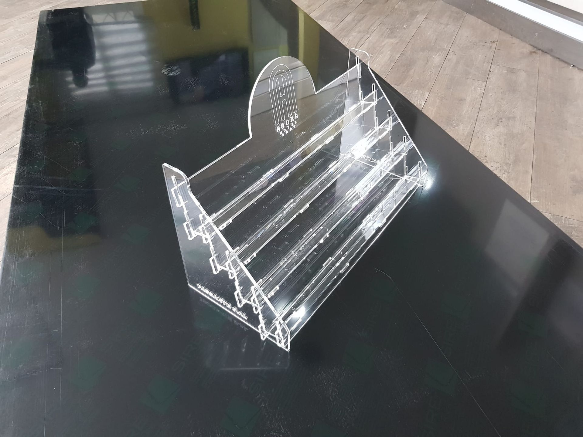 Un espositore a più livelli in acrilico trasparente, poggiato su una superficie nera lucida.