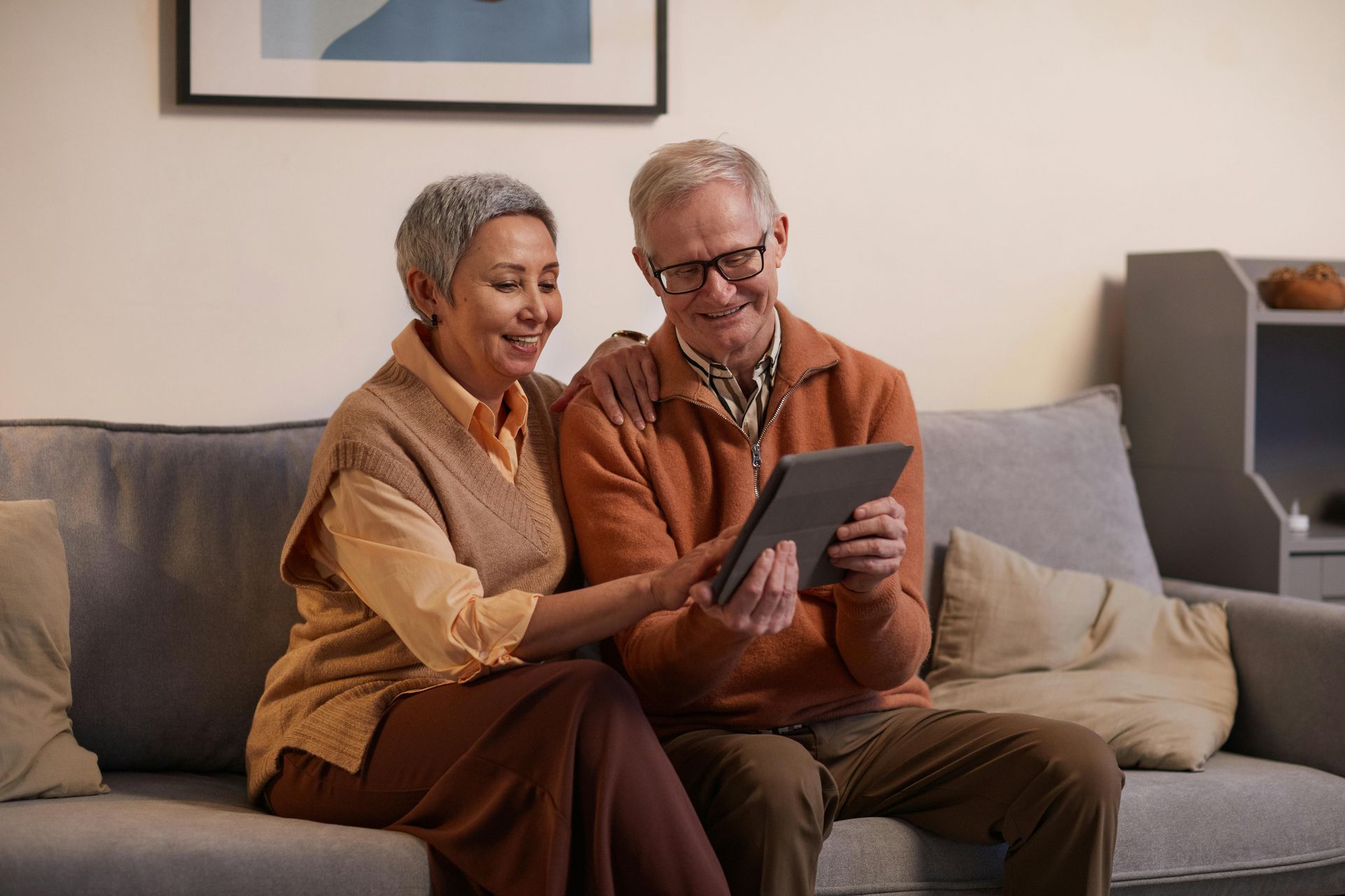 An older couple on the sofa together, looking at a tablet