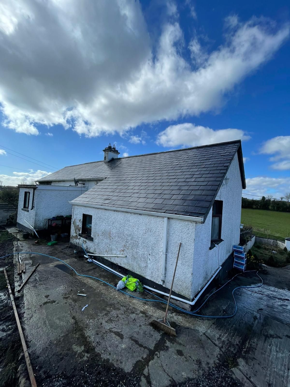A white house with a slate roof is sitting in the middle of a field.