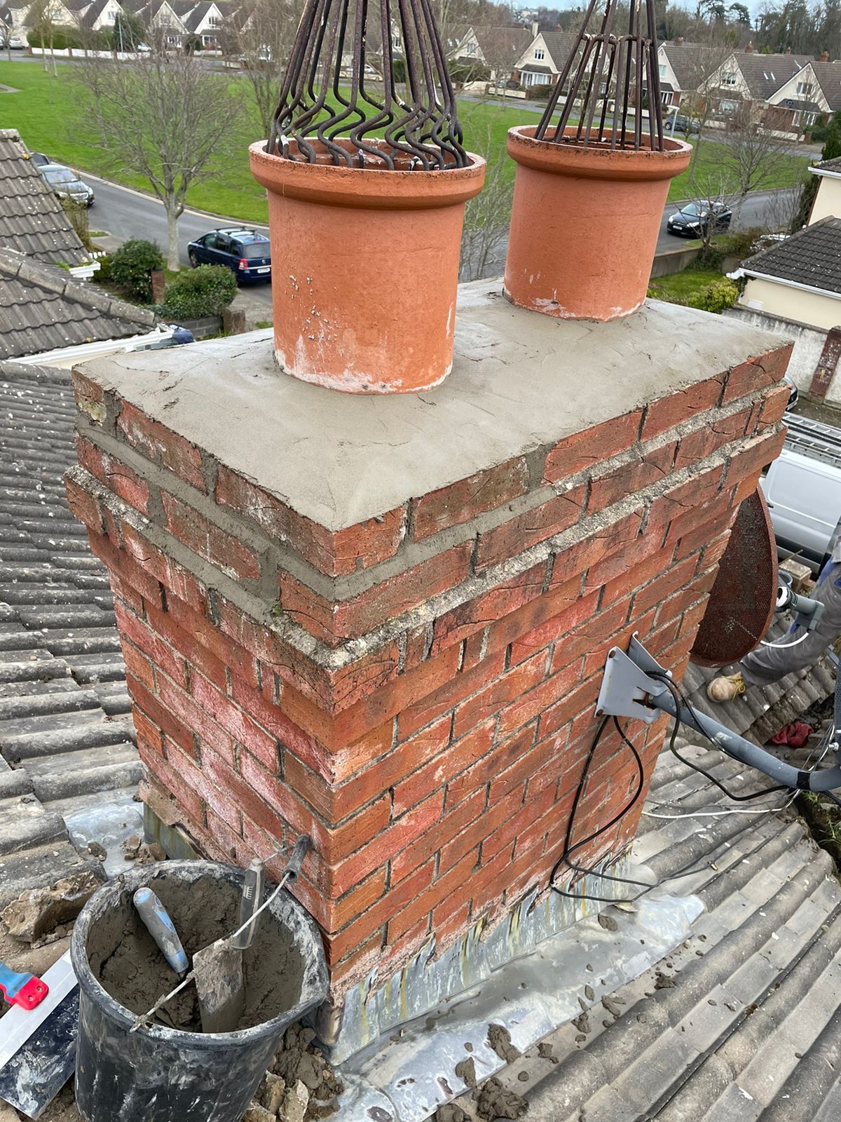 Two potted plants are sitting on top of a brick chimney.