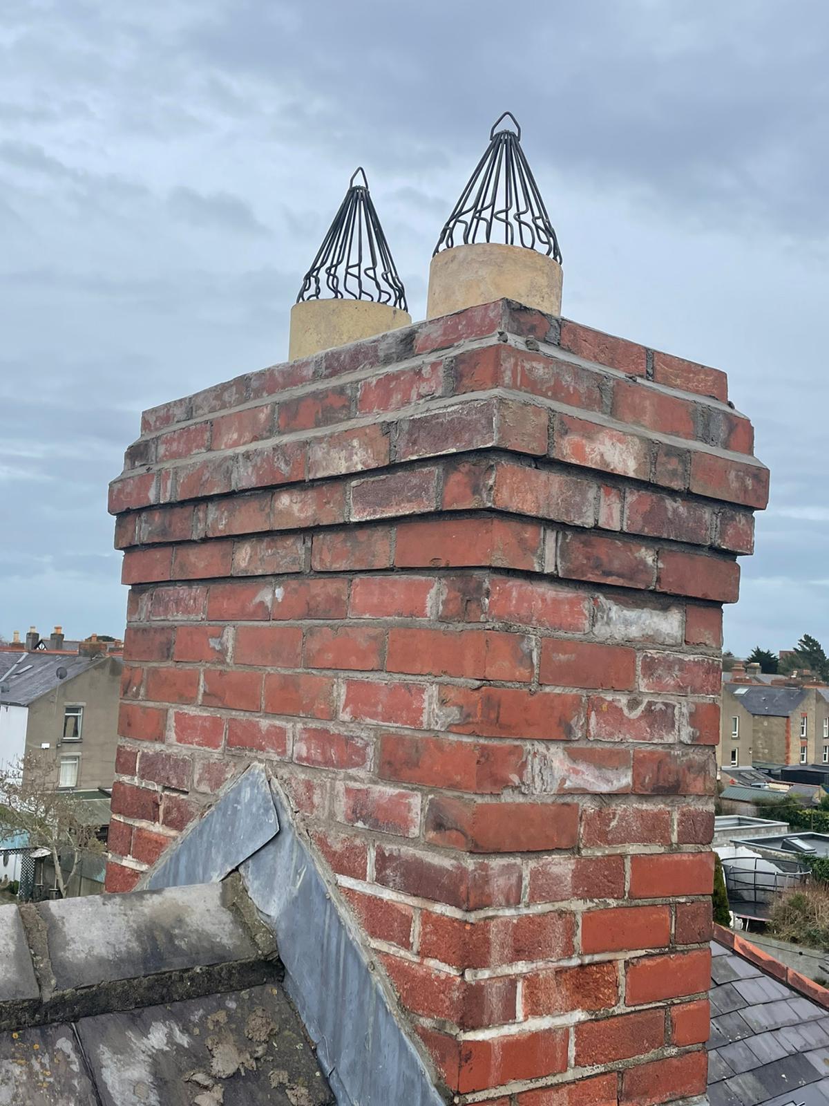 A brick chimney on top of a roof with two chimneys on top of it.