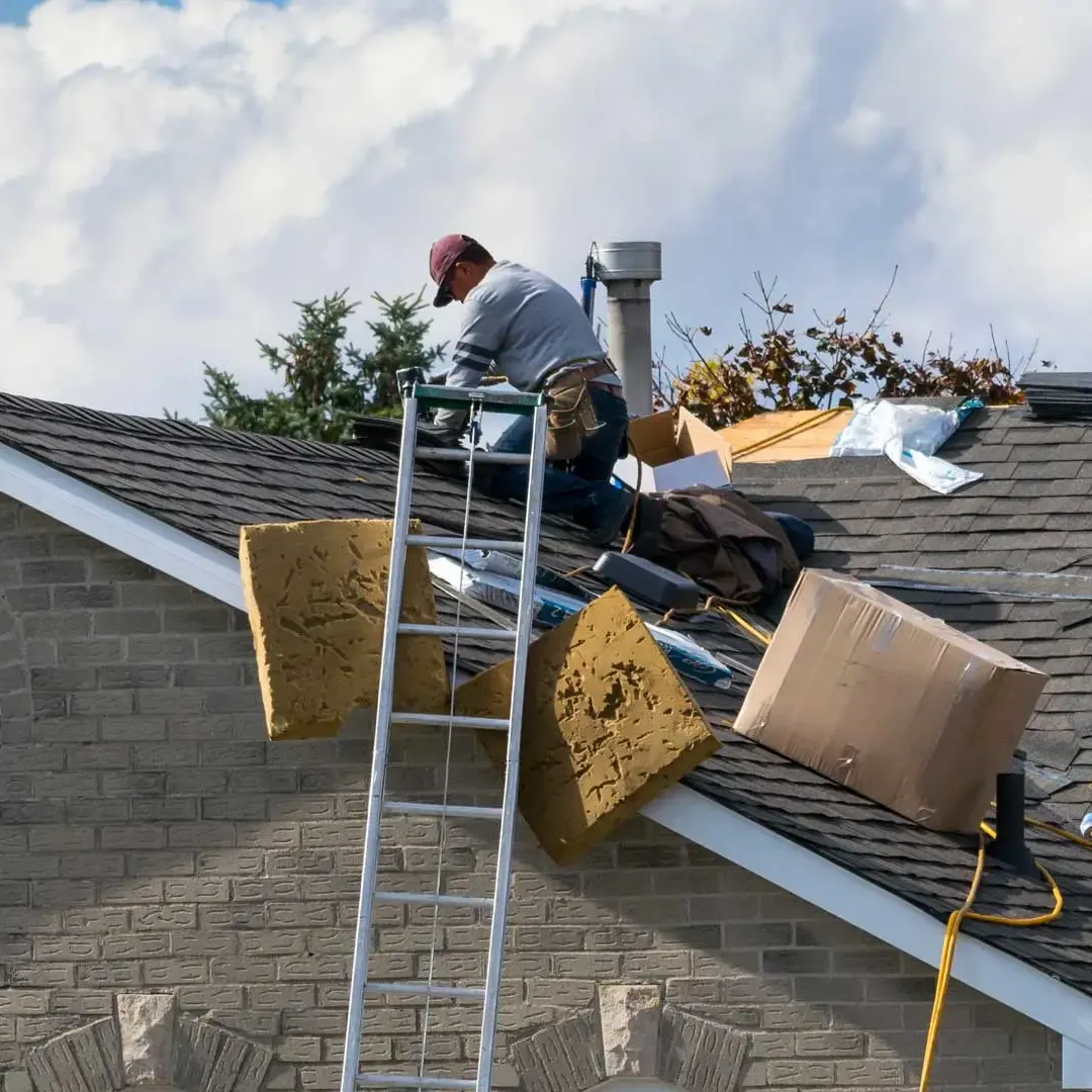 A man is working on the roof of a house with a ladder.