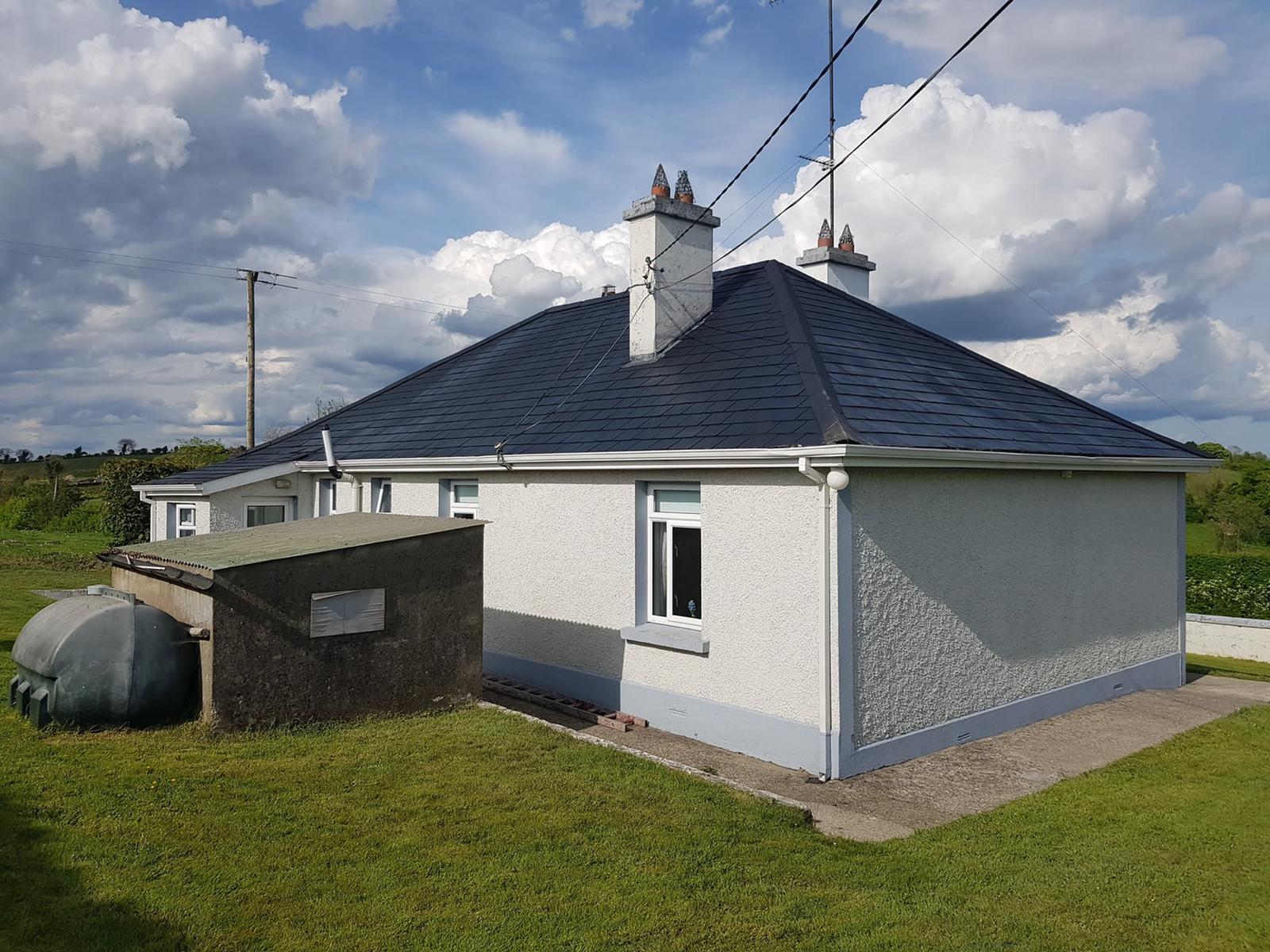 A white house with a black roof is sitting in the middle of a grassy field.