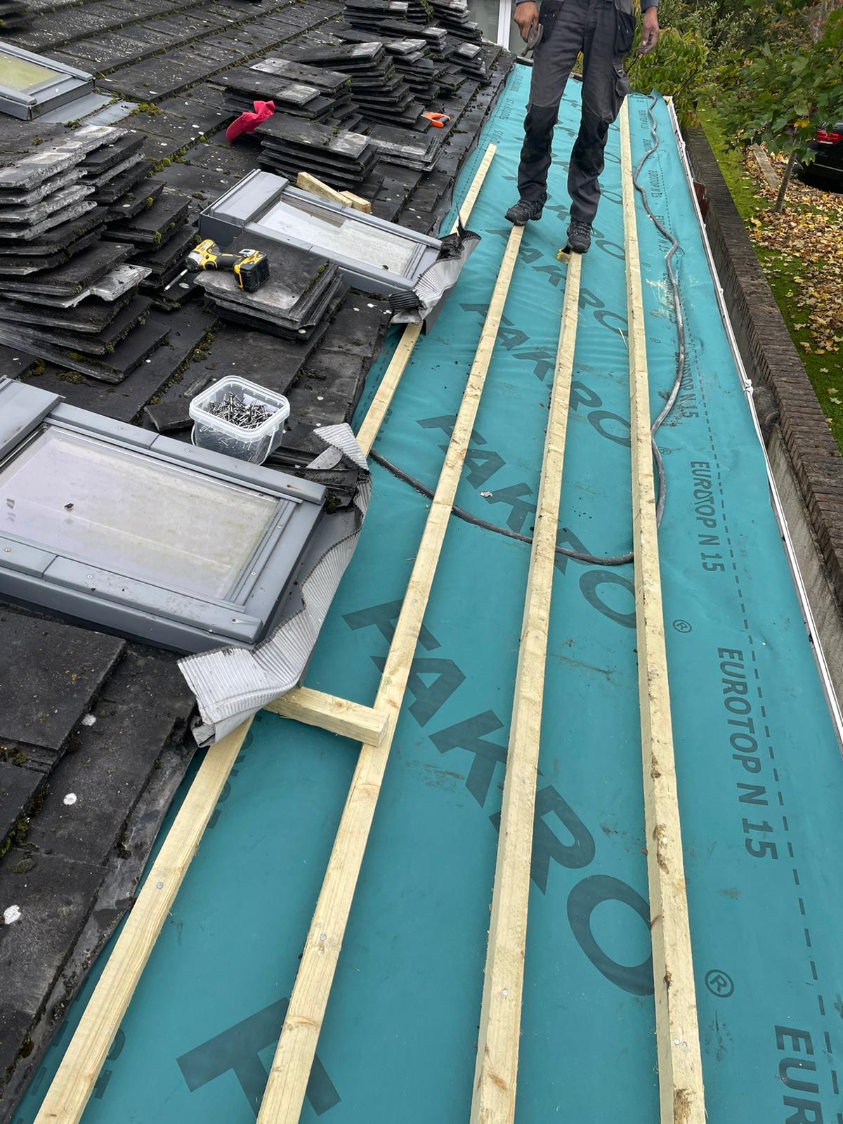 A man is standing on a roof with a green tarp on it