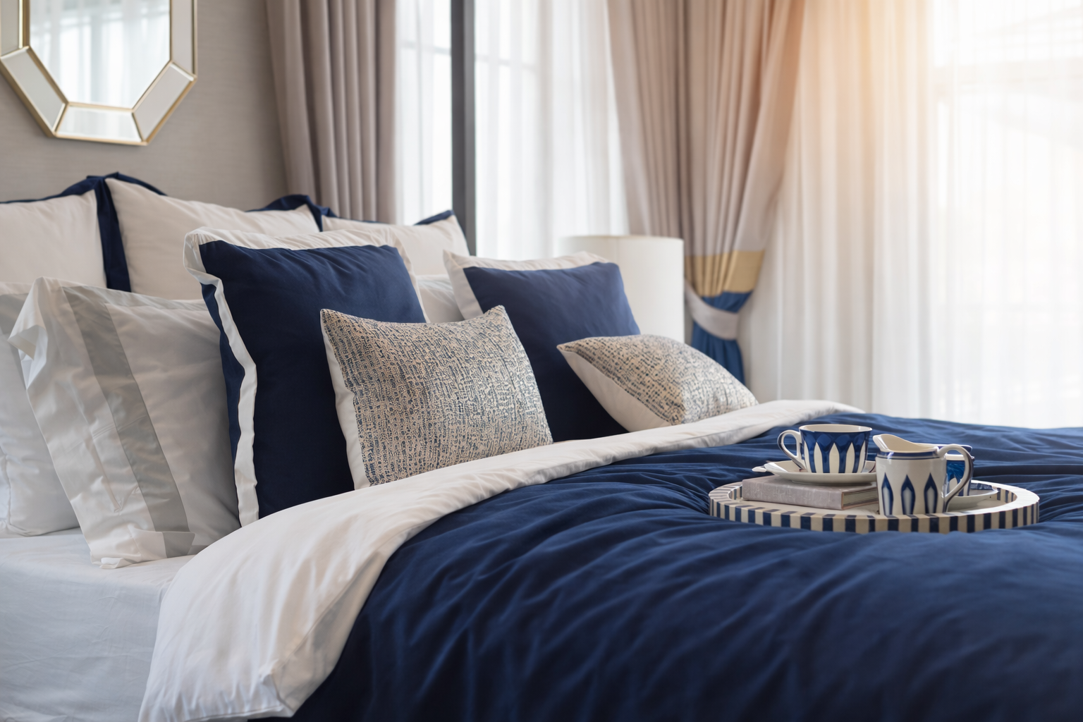 A made bed with blue and white pillows, a blue duvet, and a breakfast tray with a cup and pitcher.