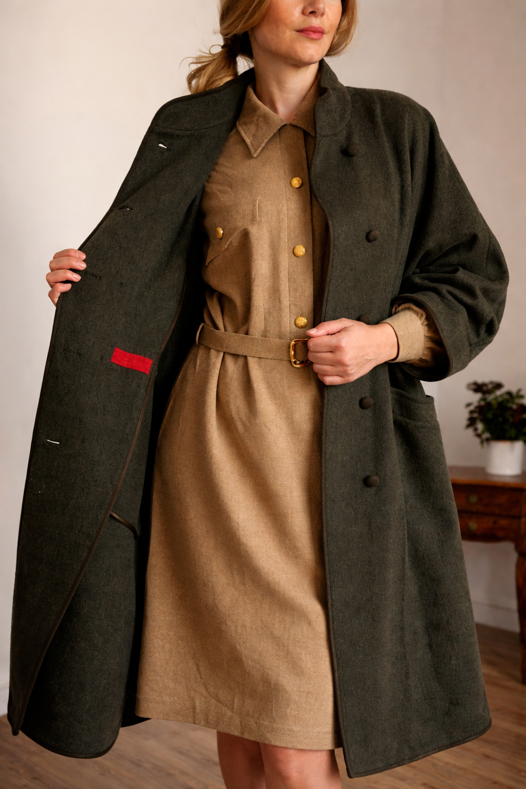 A person wearing a dark green wool coat over a tan belted dress, showing the open coat's interior.