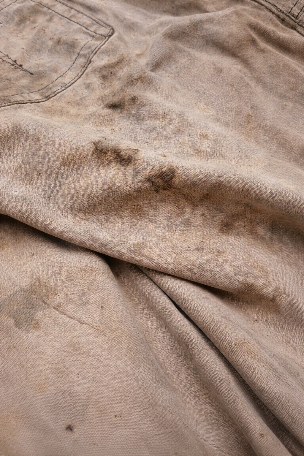 Close-up of tan fabric with various dark stains and smudges on a wrinkled surface.