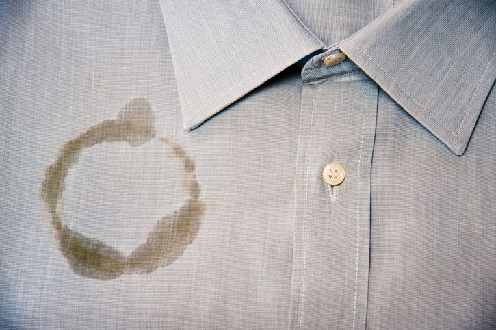 A light gray button-down shirt with a prominent, circular brown coffee stain on the left side of the chest.