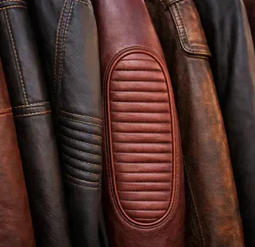 A close-up of several brown and black leather jackets hanging side-by-side, highlighting textures and ribbed detailing.