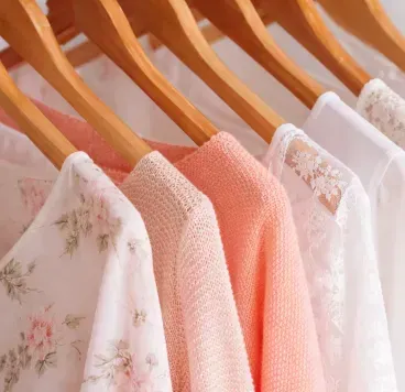 Several light-colored shirts and cardigans with floral, textured, and lace patterns hanging on wooden hangers.
