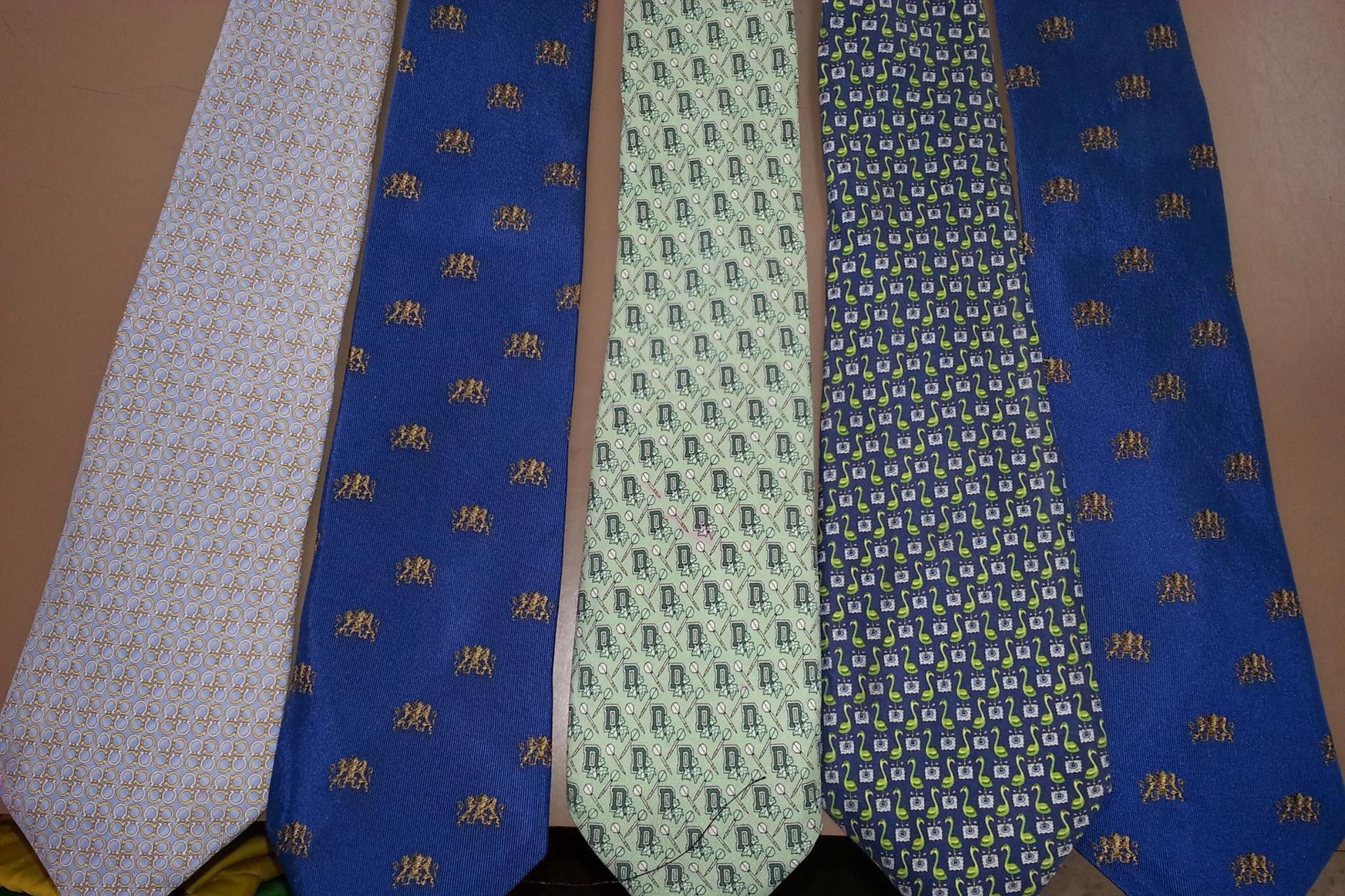 Five men's neckties with various patterns and colors—light grey, blue, pale green, and dark navy—laid side-by-side.