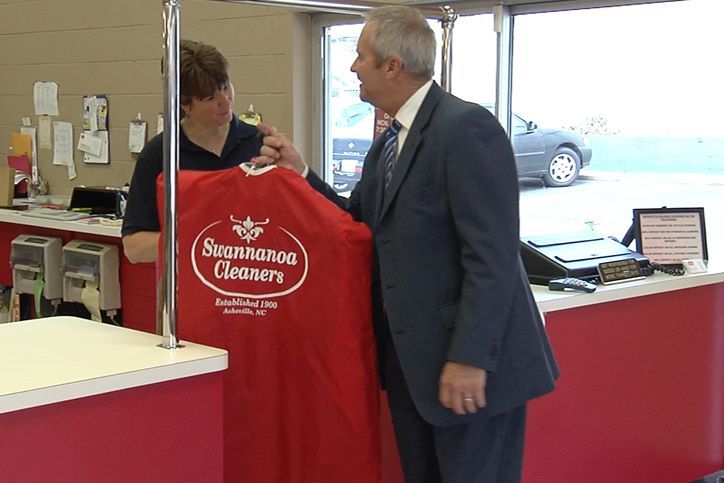 A person in a suit hands a red garment bag with the 