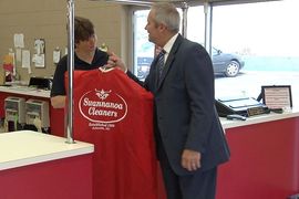 A person in a suit hands a red garment bag with the