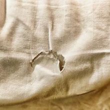 A light-colored fabric with a noticeable, jagged hole in the center.