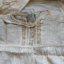 A white vintage garment with a high collar, delicate lace panels, and intricate vertical pintuck detailing.