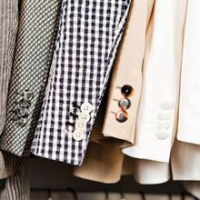 A row of blazers hanging on a rack, featuring various patterns and colors including gingham, beige, and white.