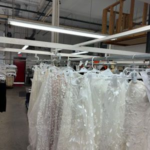 A row of white lace wedding dresses hanging on a metal rack in an industrial-style studio or warehouse space.