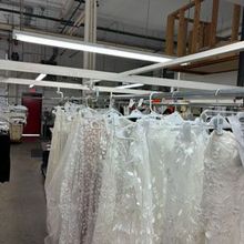 A row of white lace wedding dresses hanging on a metal rack in an industrial-style studio or warehouse space.