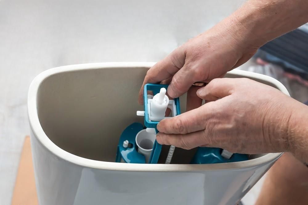 A person is fixing a toilet tank with their hands.