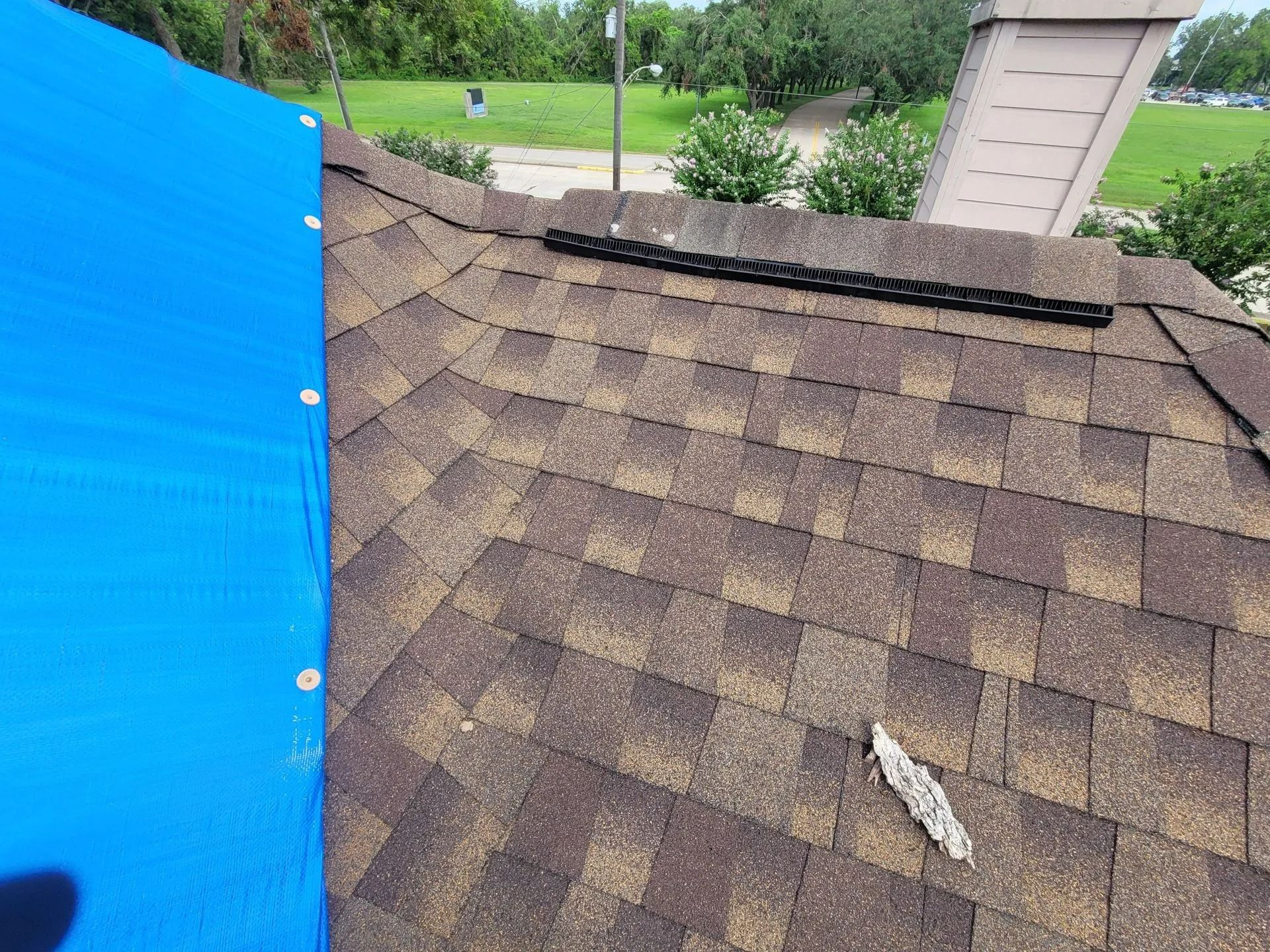 Blue tarp covers a section of a brown shingled roof, likely to protect from damage.