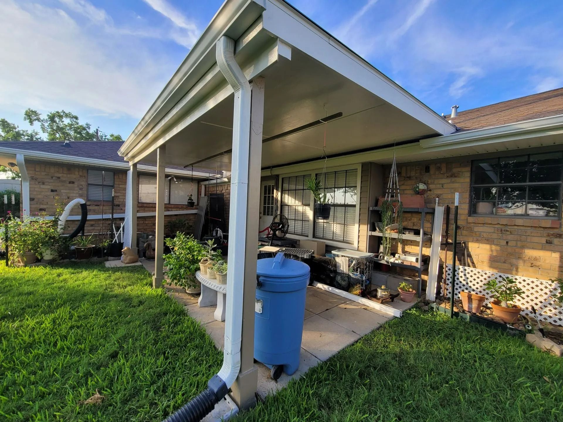 Backyard patio with a blue trash can, brick house, and green grass.