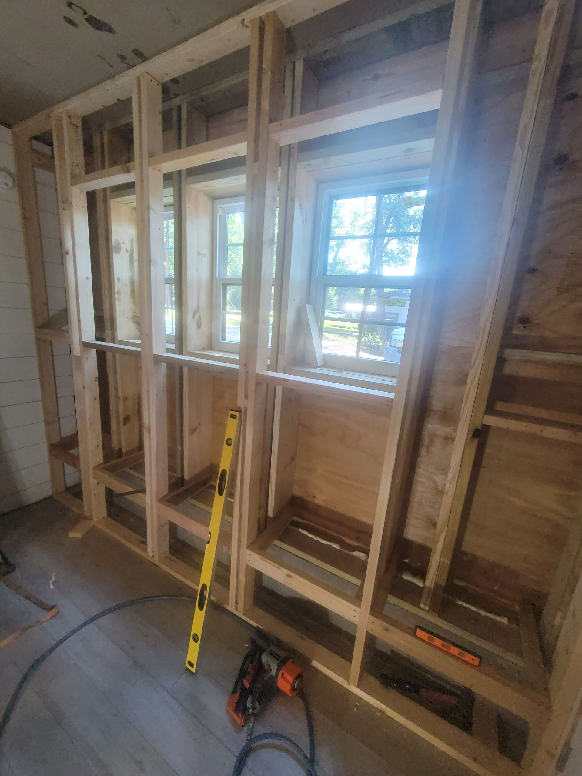 Wooden frame structure built around windows, with level and tools on floor.