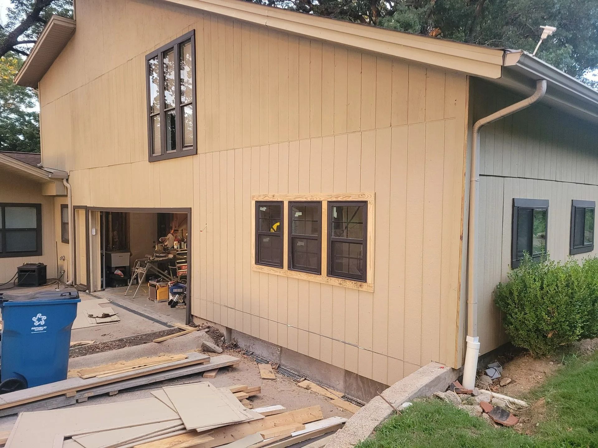 Beige house with a garage and multiple windows, with construction materials in the foreground.