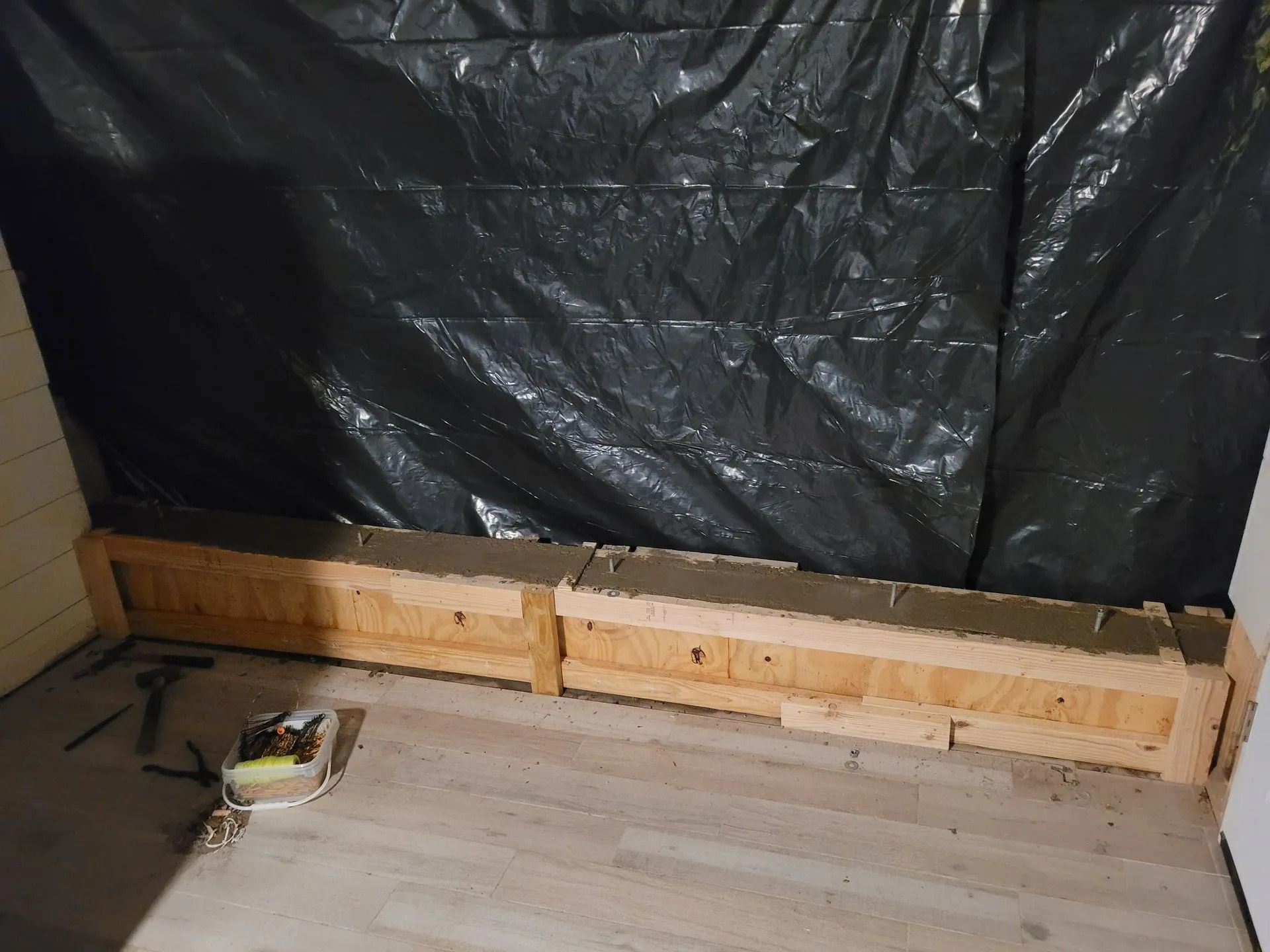 Wooden boxes along a wall covered with black plastic sheeting. Tools rest on the light-colored floor.
