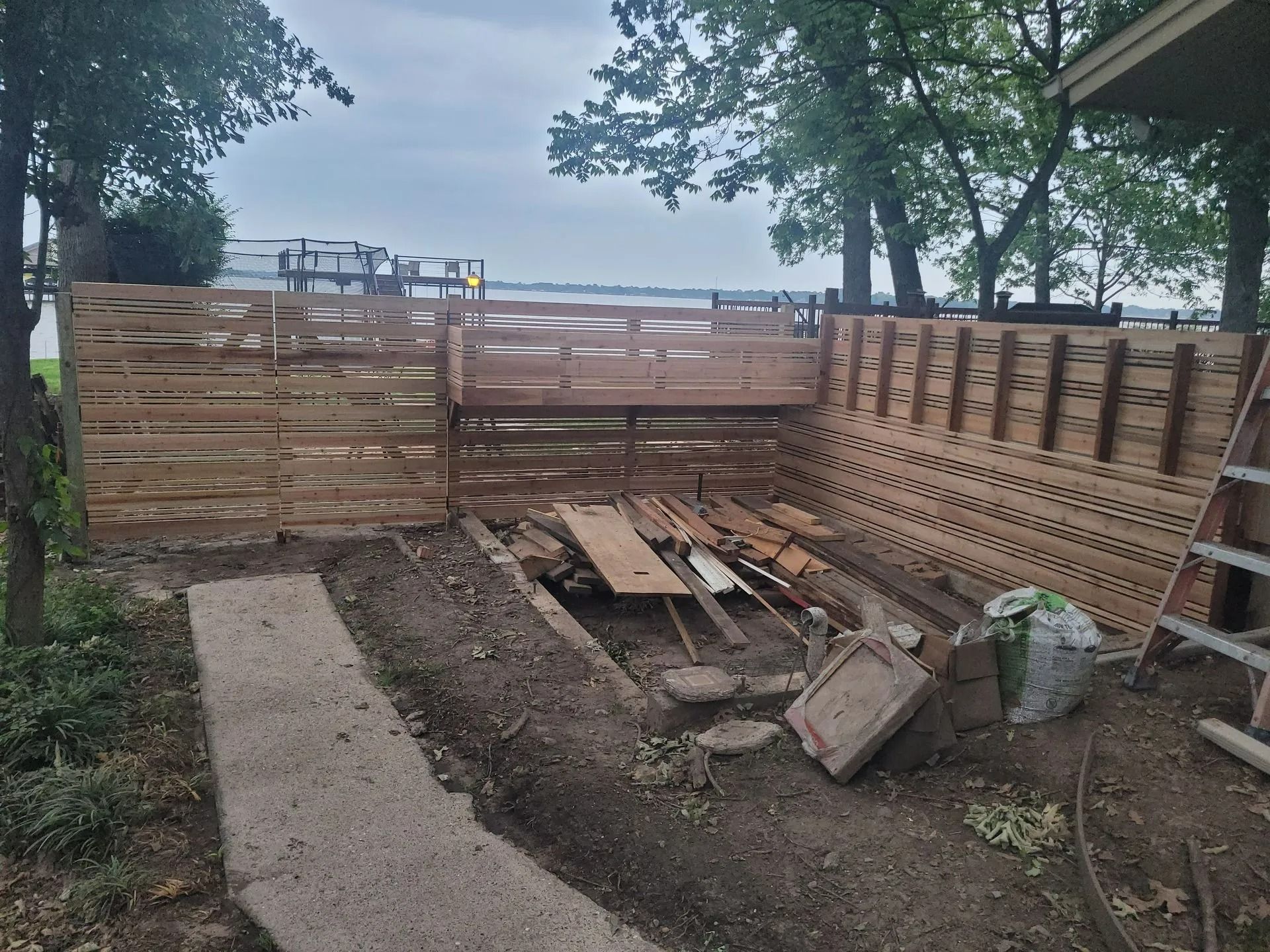 Wooden fence construction site near water, with debris and exposed ground.