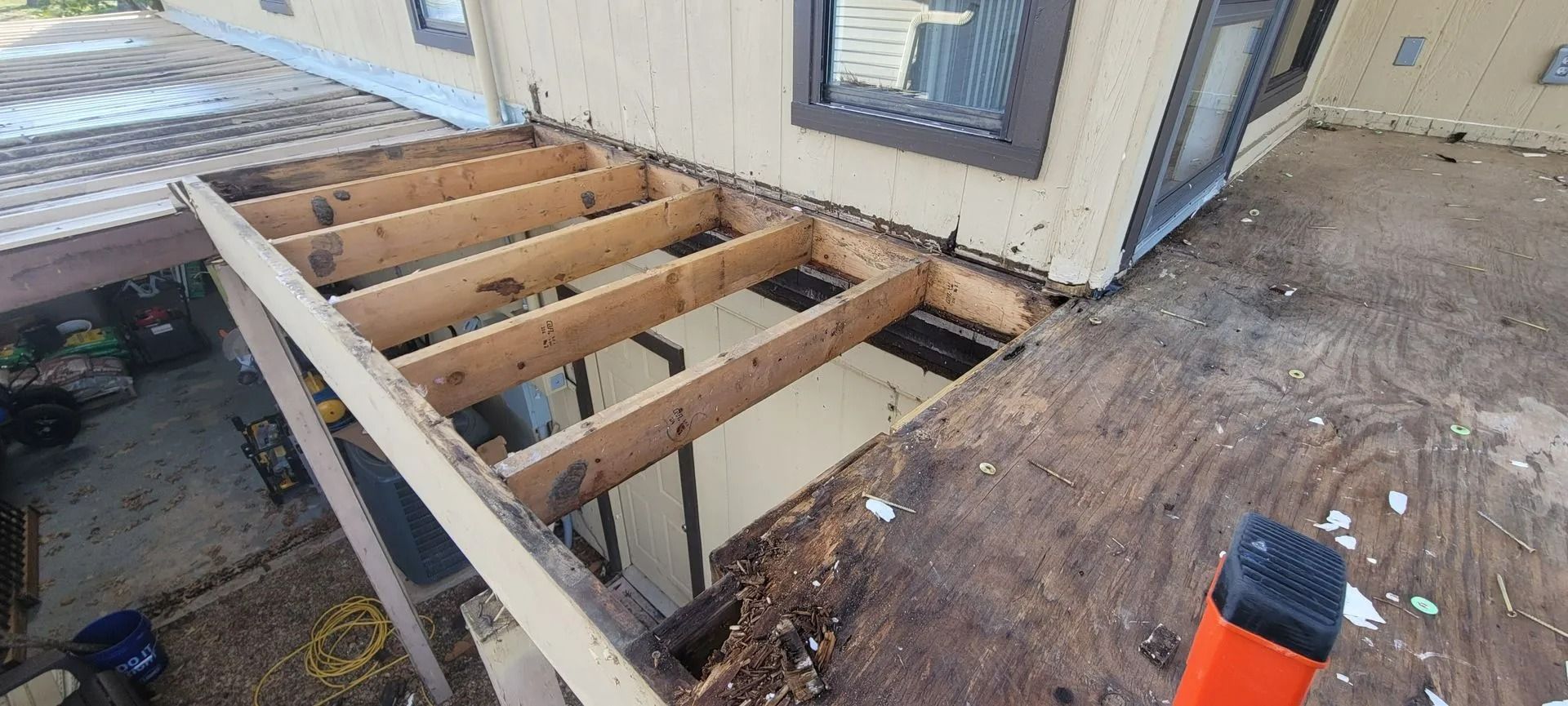 A partially dismantled wooden deck with exposed joists near a house wall.