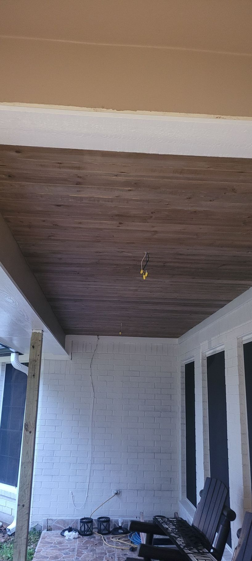 Wooden porch ceiling with a light fixture, white brick wall, and bench.